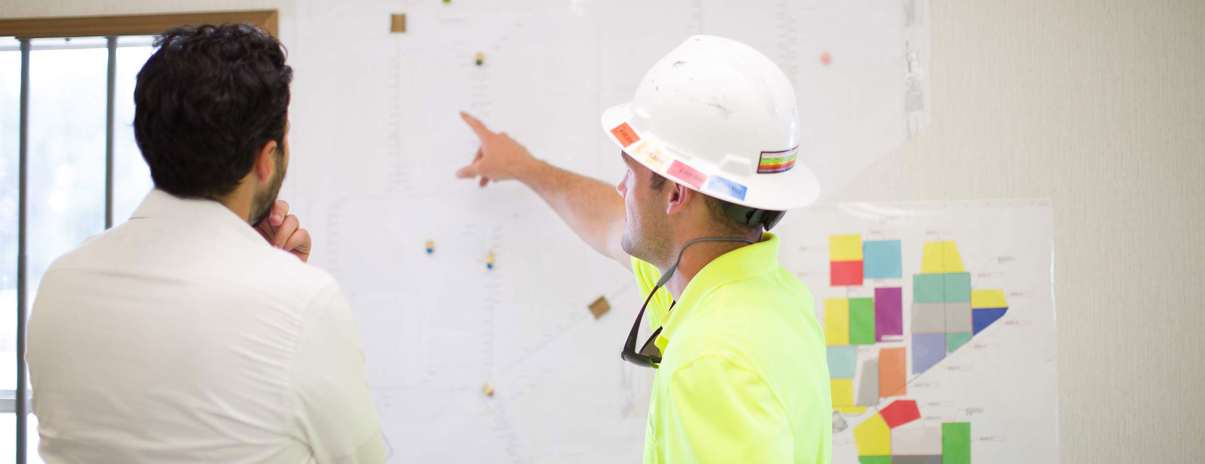 Two employees looking at plans on a wall